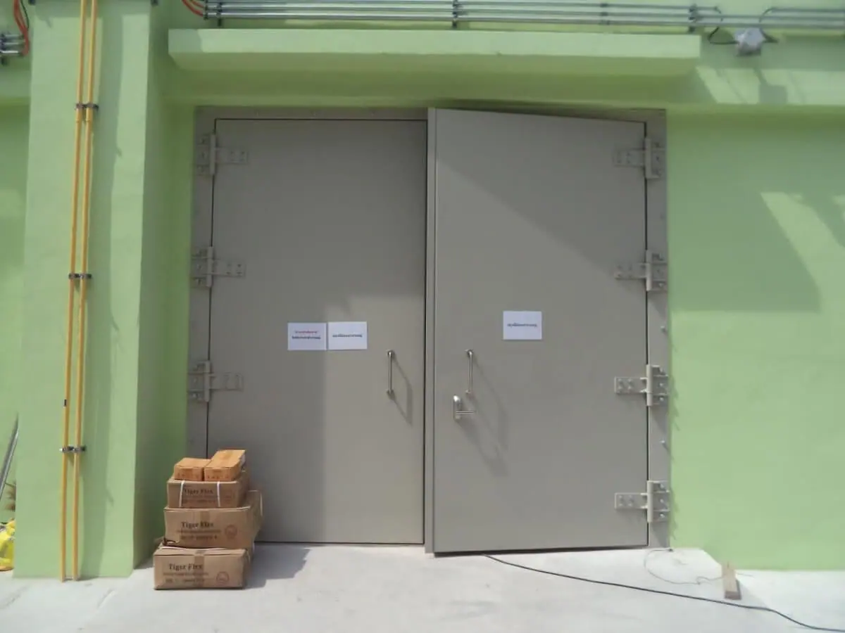 Beige double leaf blast doors on a green wall with one leaf slightly open