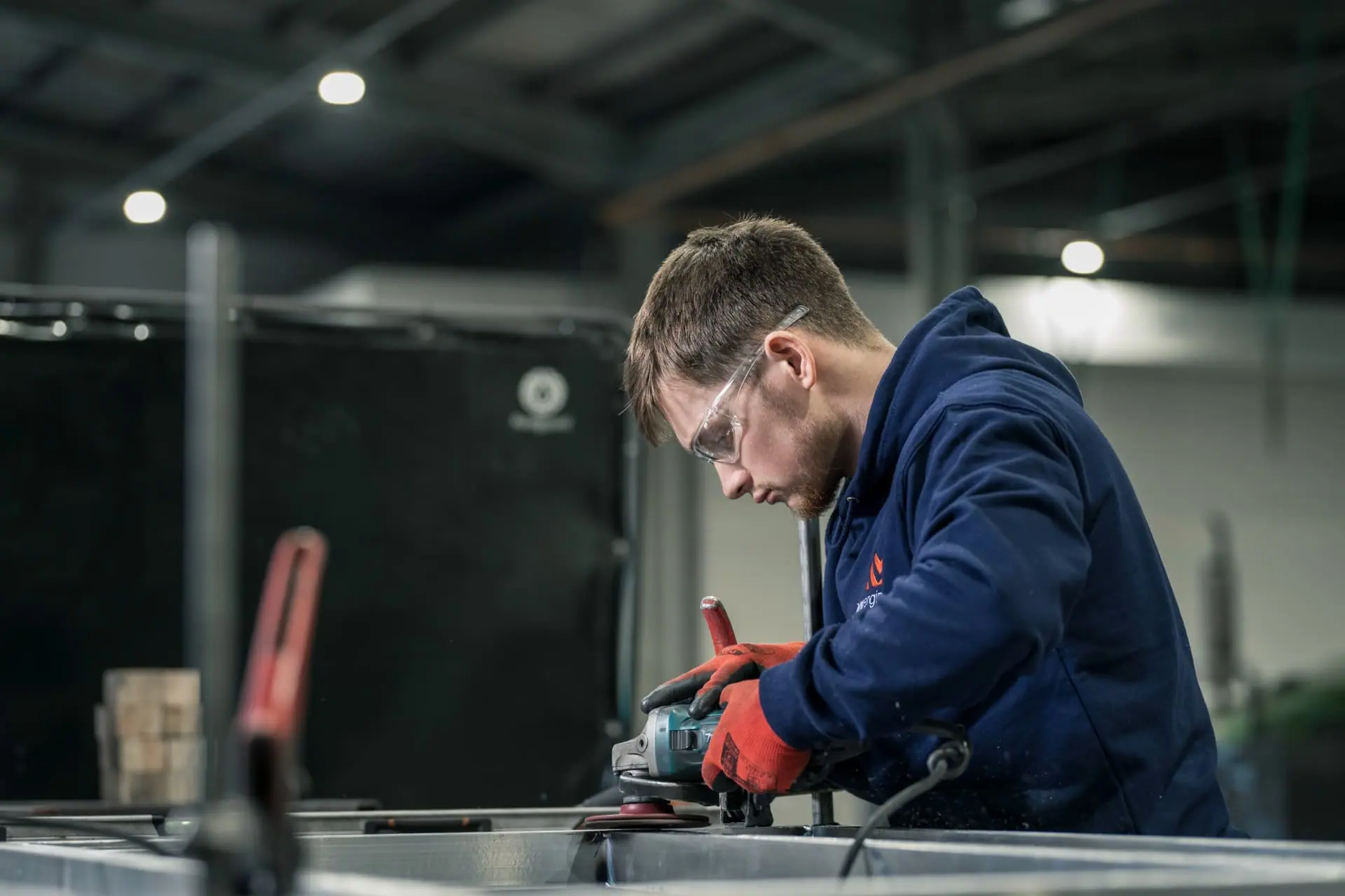 Fabricator in safety glasses grinding a steel component in the MM Engineering workshop