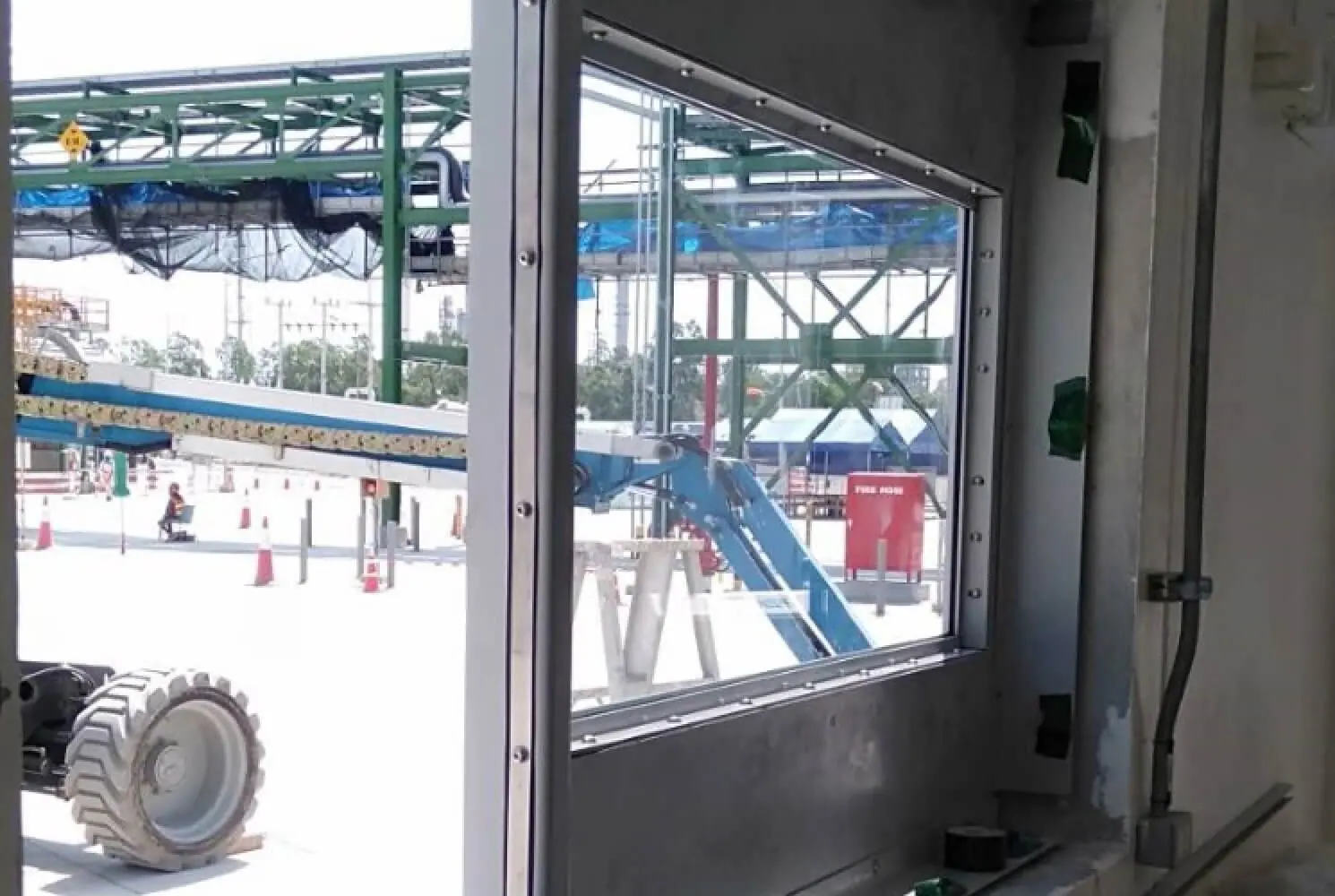 Blast window frame with glazing installed, overlooking an industrial plant with pipework