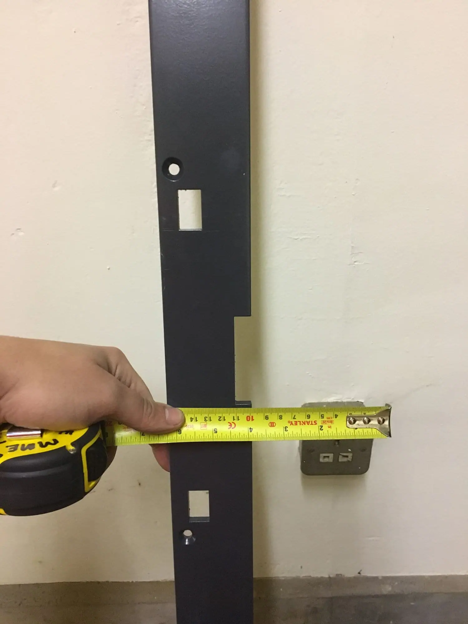 Dark grey steel door leaf plate with cut-outs being measured with a tape