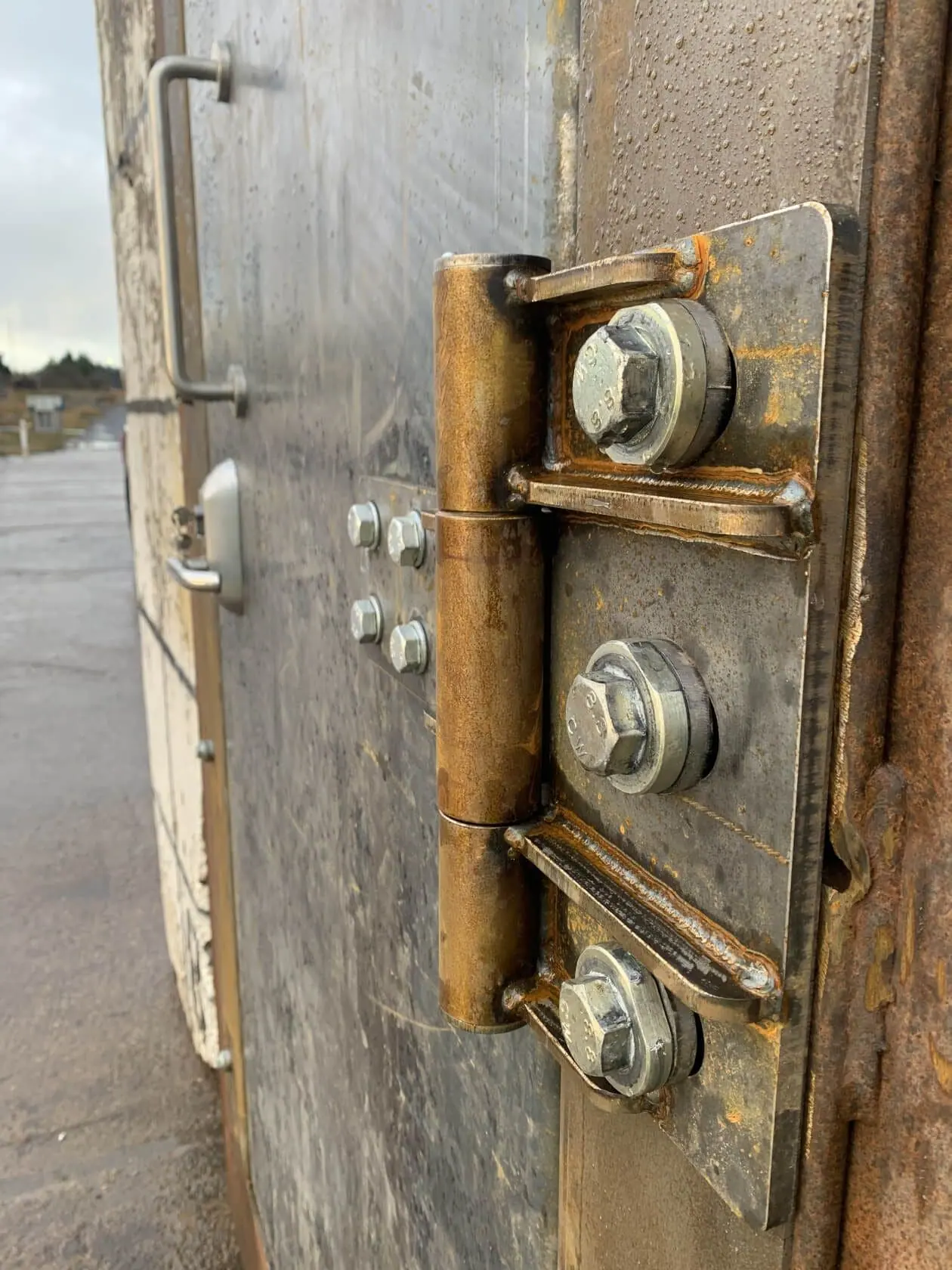 Close-up of a blast door hinge with welded brackets and large bolts