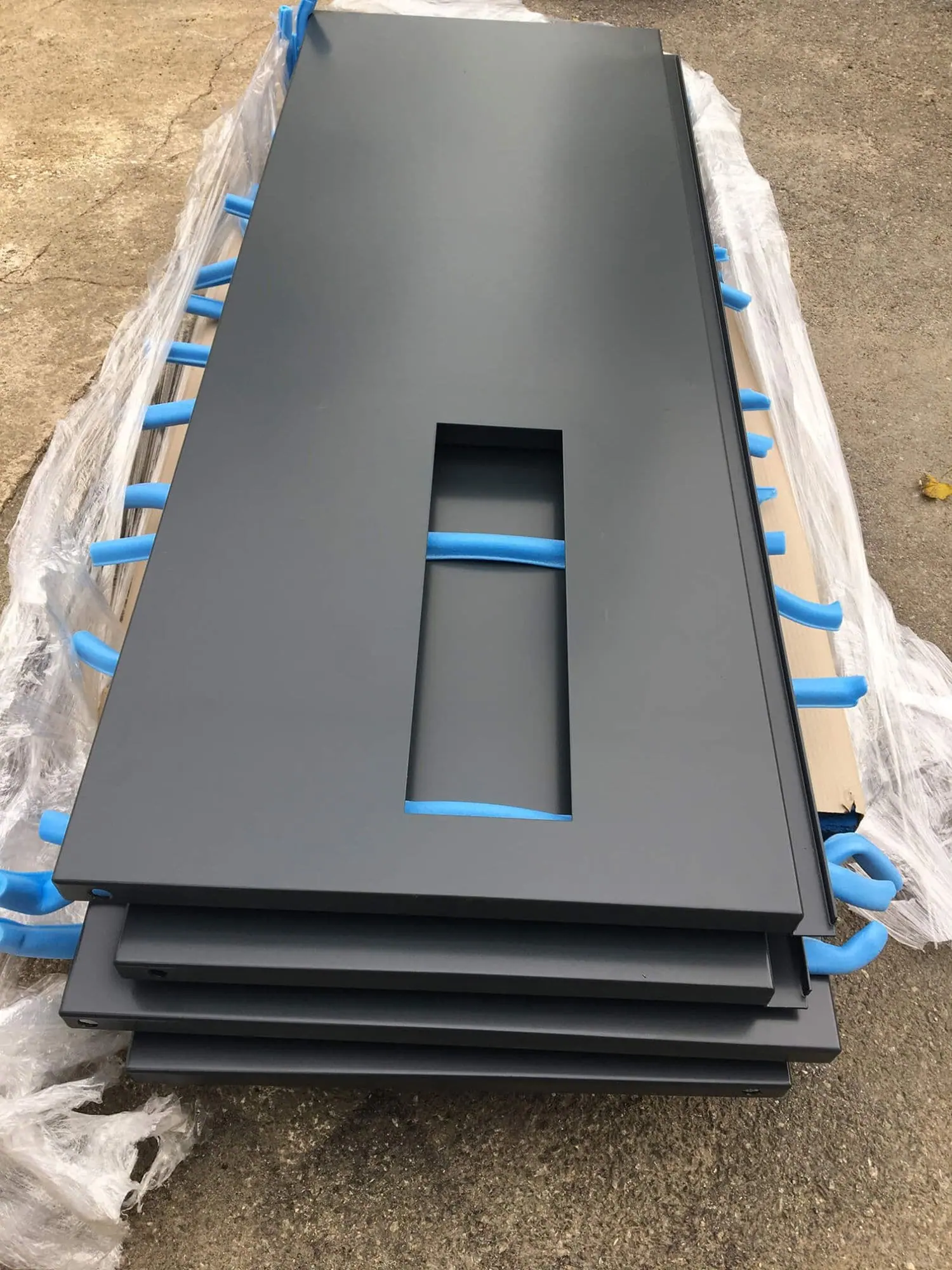 Stack of grey powder-coated flood door panels wrapped in plastic and blue foam