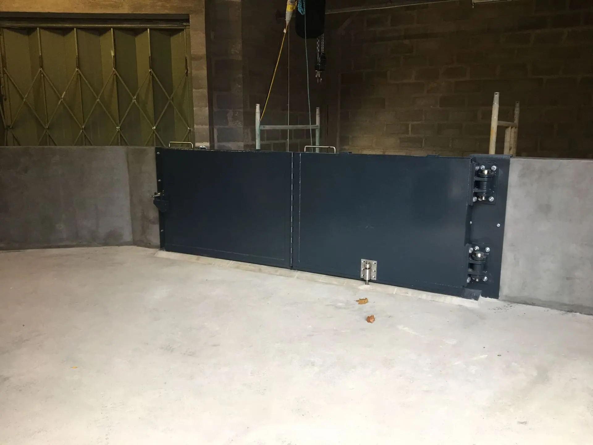 Closed bifold dark blue flood gate with stainless steel hinges set between concrete walls
