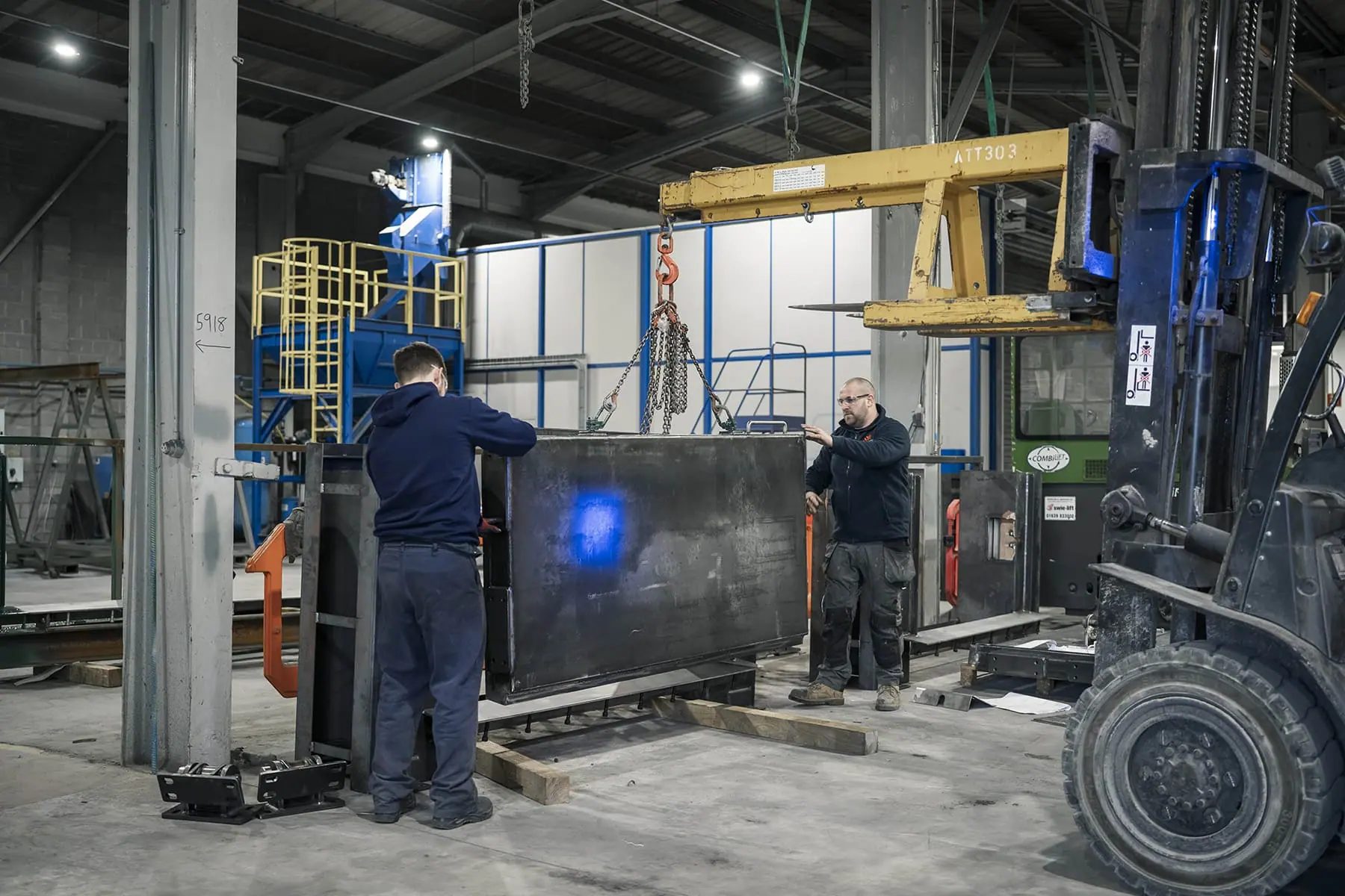 Two workers positioning a large steel door leaf lifted by chains in the factory