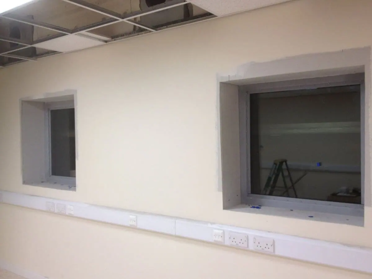 Two blast windows with grey frames fitted into an interior wall above power sockets