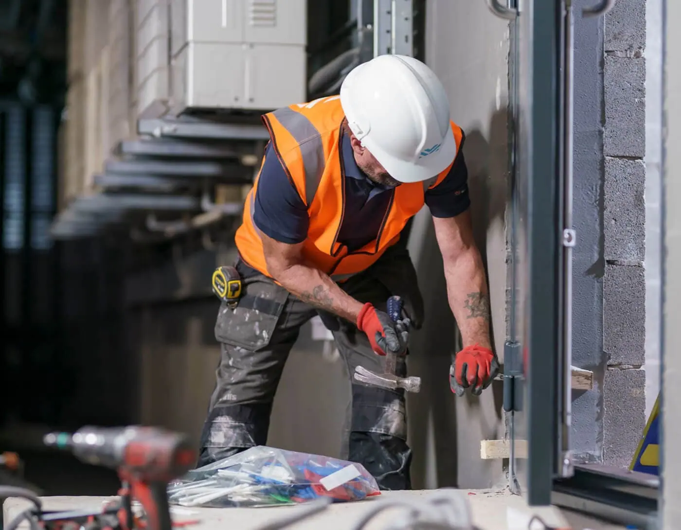 Installer in hard hat and hi-vis fitting a door frame with a hammer on site