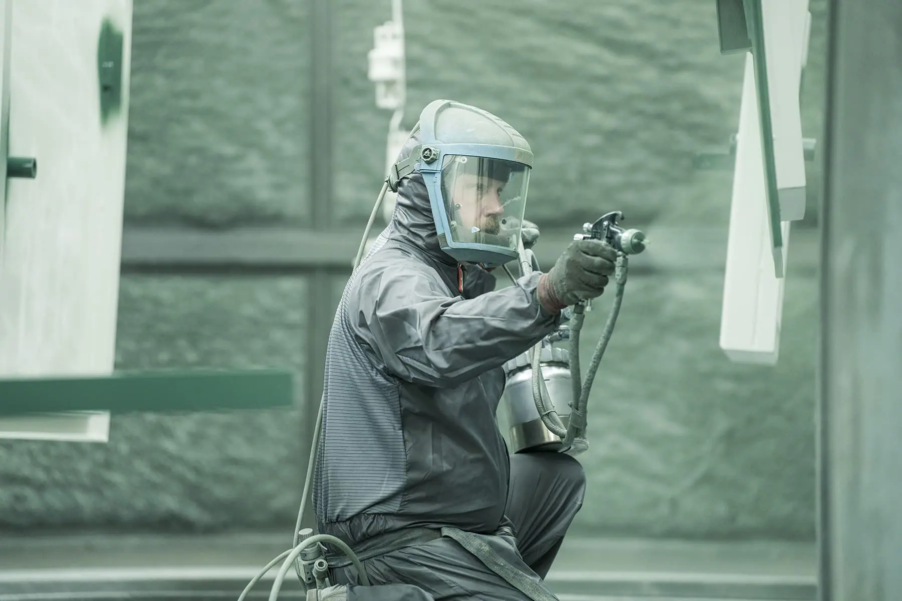 Operative in respirator hood and protective suit spray painting steel door components in a booth