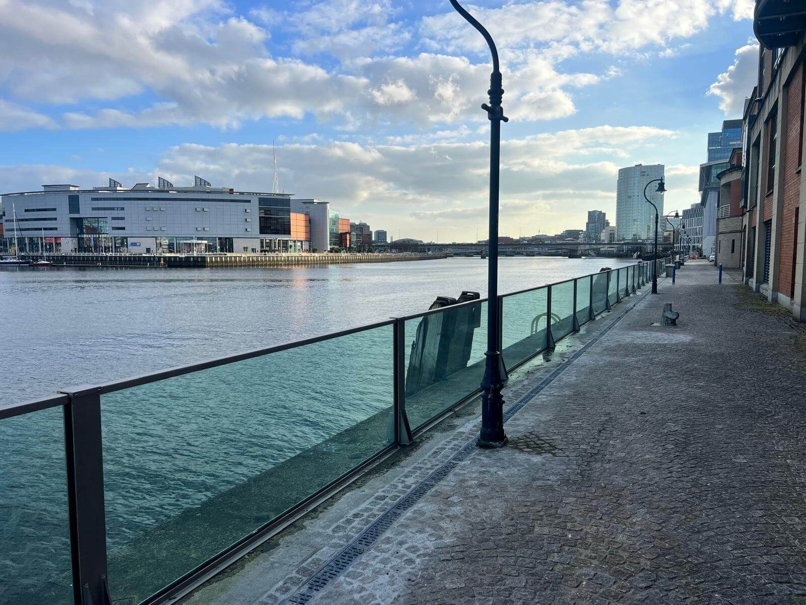 Long run of glass flood barrier panels along a river quay with street lamp