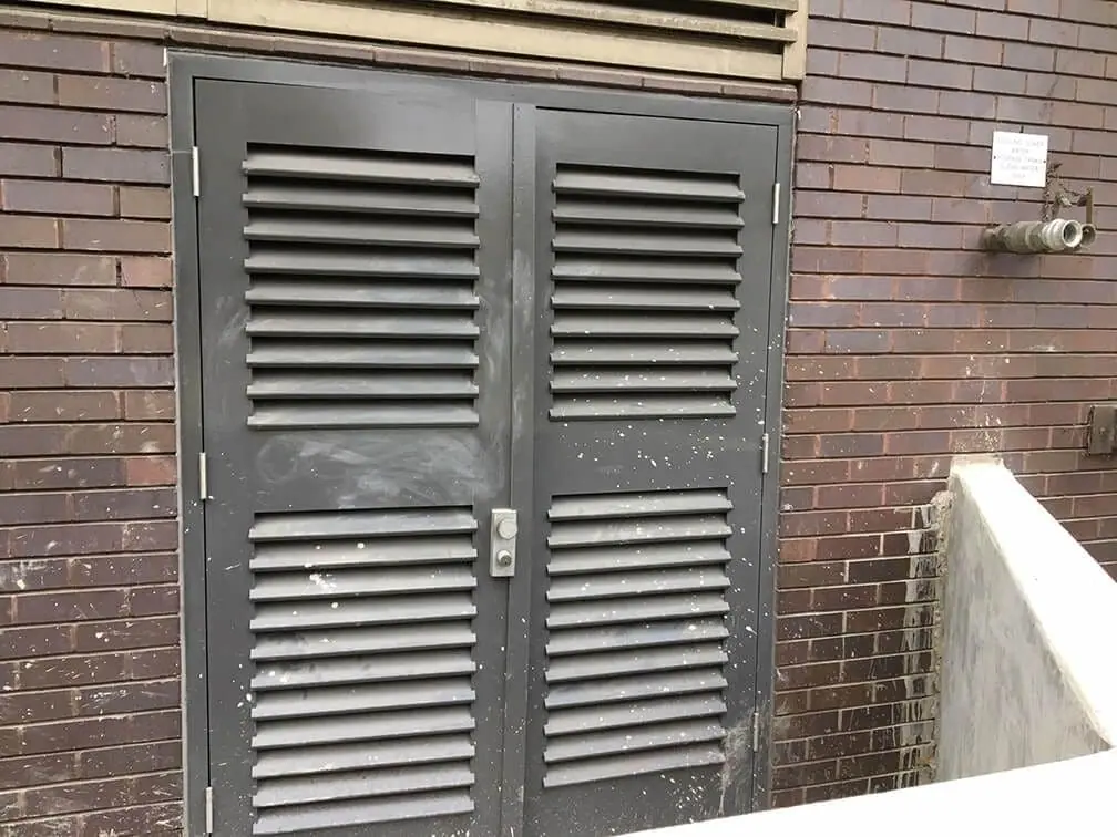 Louvred double doors in a brick wall beside a concrete flood wall