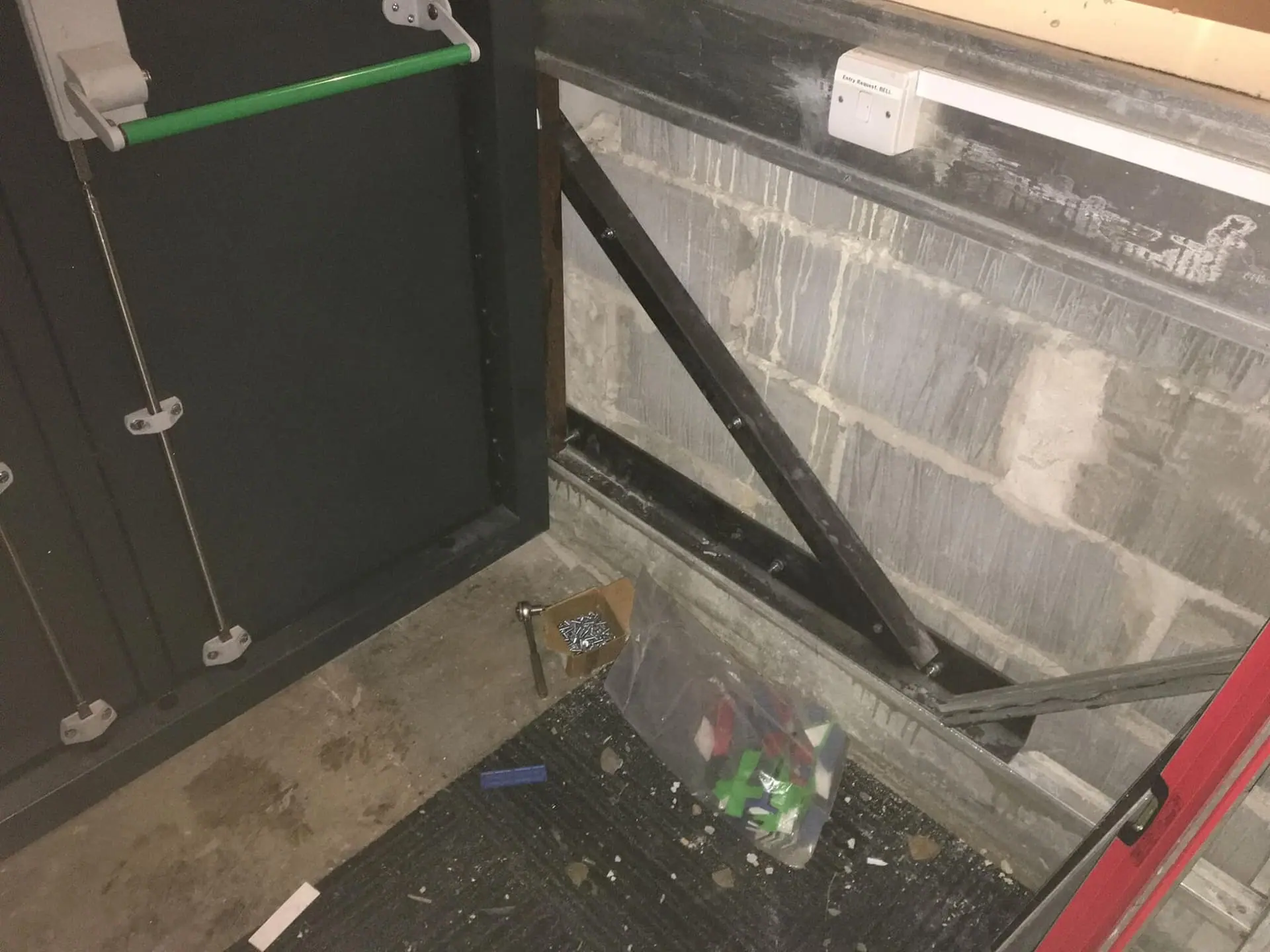 Rear of an open door showing steel bracing, screws and tools beside a block wall