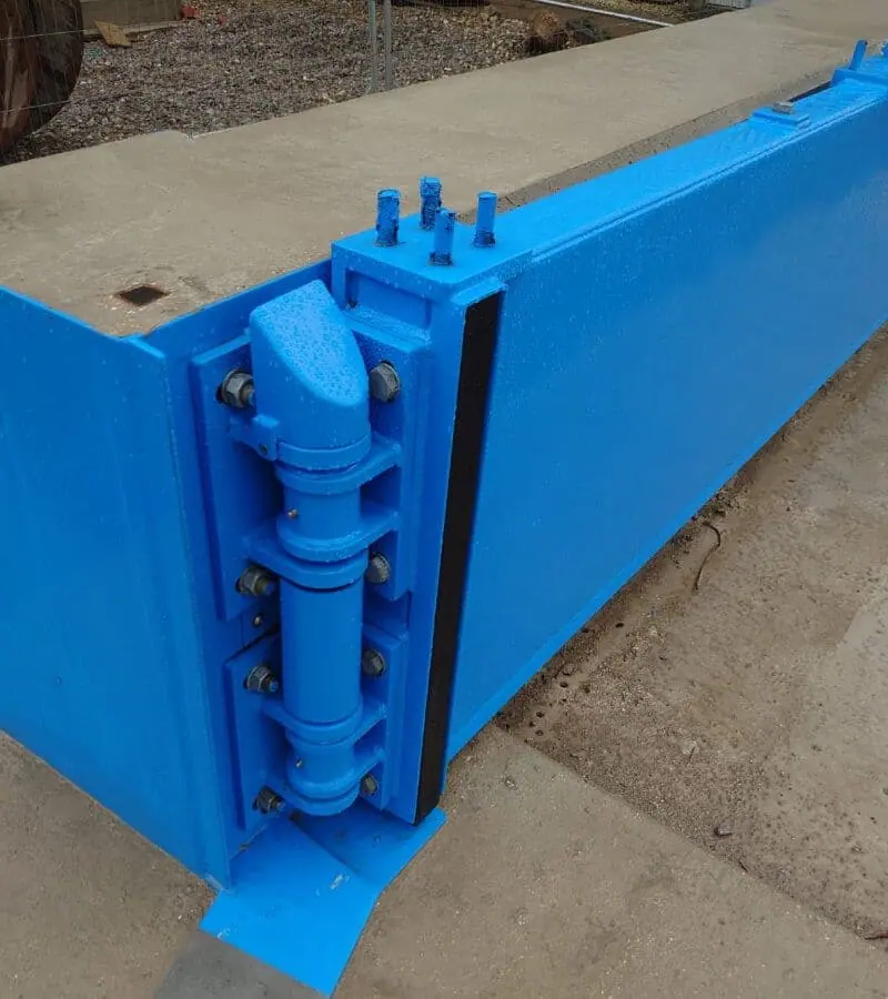 Blue steel flood gate with hinge assembly and black seal fitted across an opening