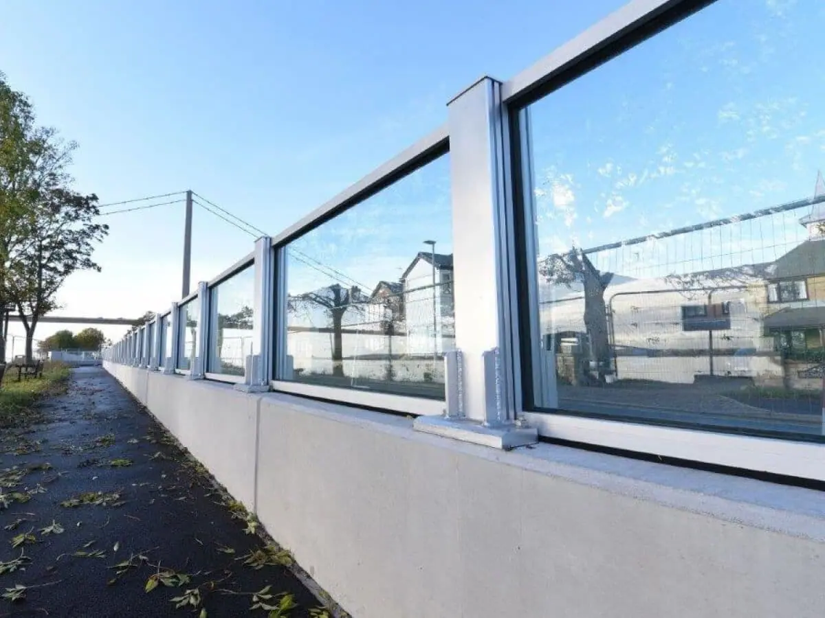 Glass flood wall panels set between aluminium posts on a concrete wall under a blue sky