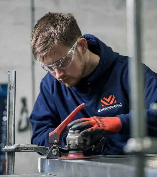 MM Engineering fabricator in safety glasses grinding an aluminium section in the workshop