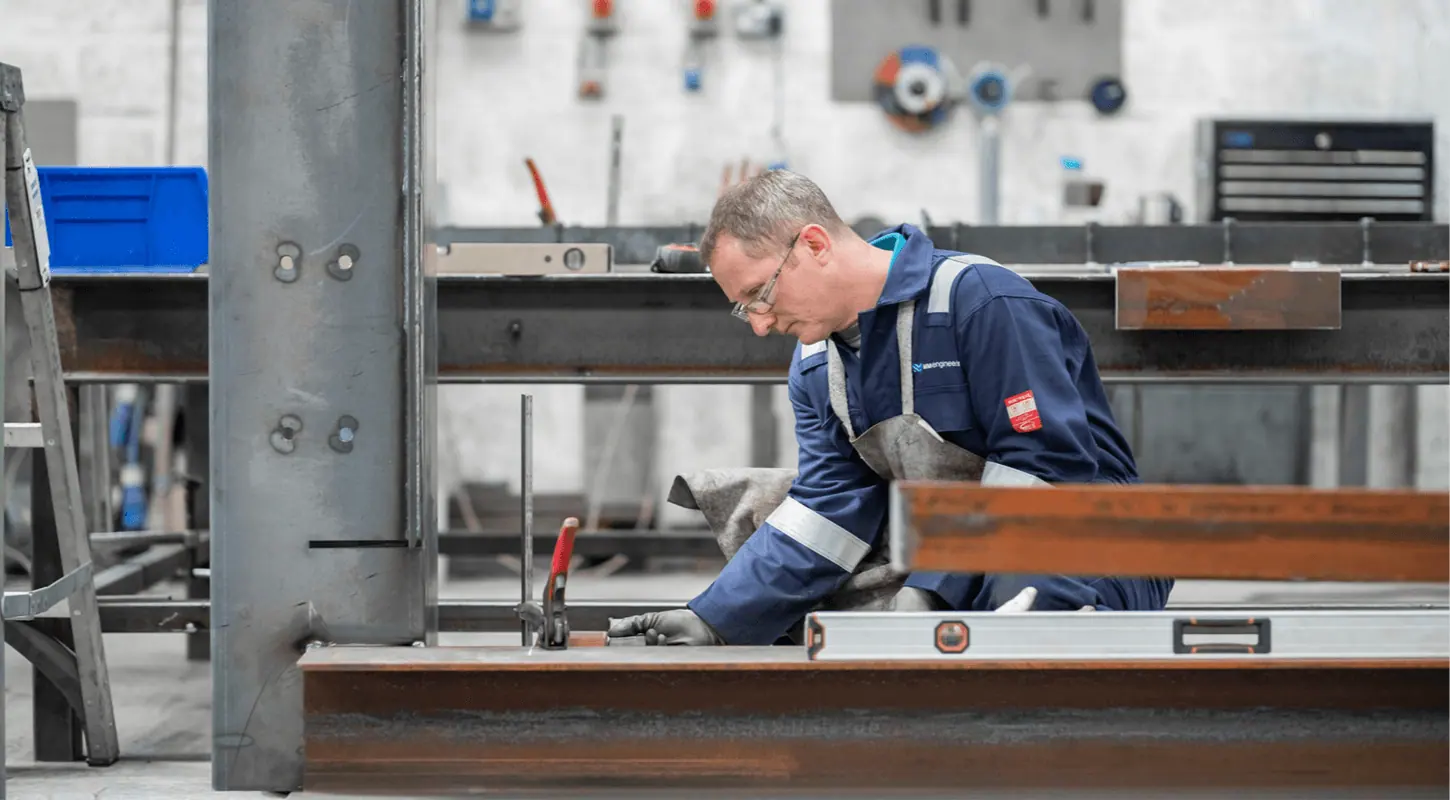 Engineer in MM Engineering overalls levelling a steel beam in the fabrication workshop