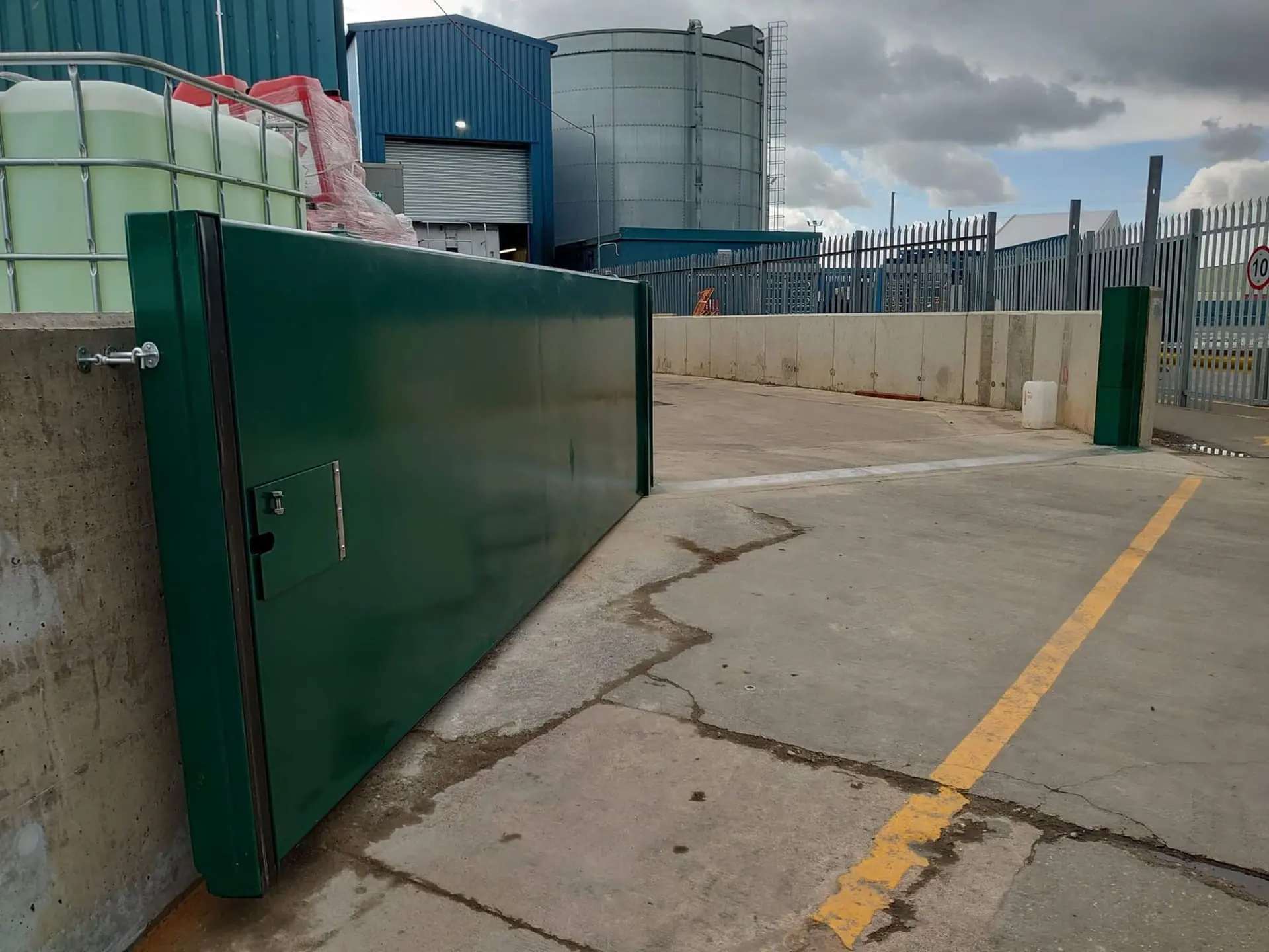 Single green flood gate leaf swung open across a concrete threshold at an industrial site