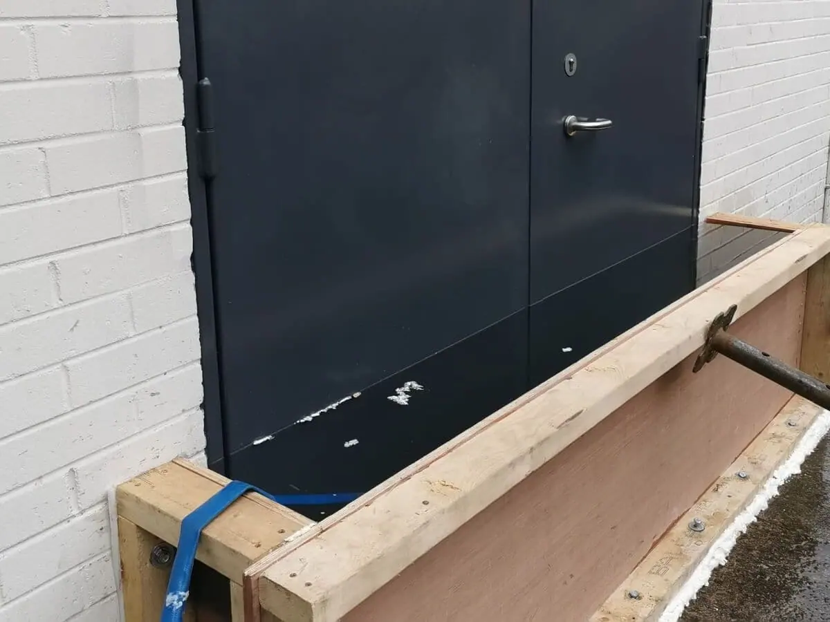 Dark grey double flood door being tested behind a timber water-filled test box
