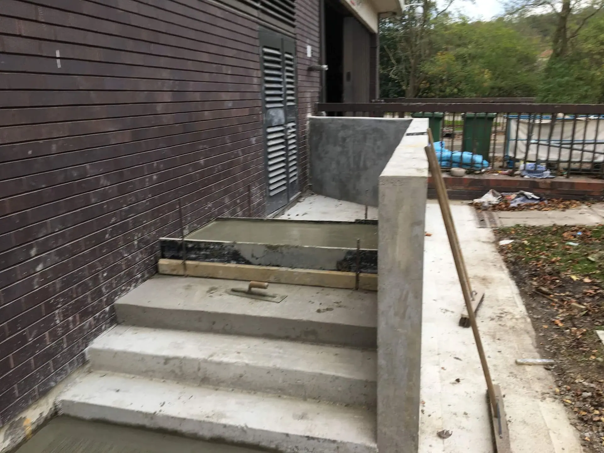 Concrete steps and flood wall under construction beside a brick building with louvred doors