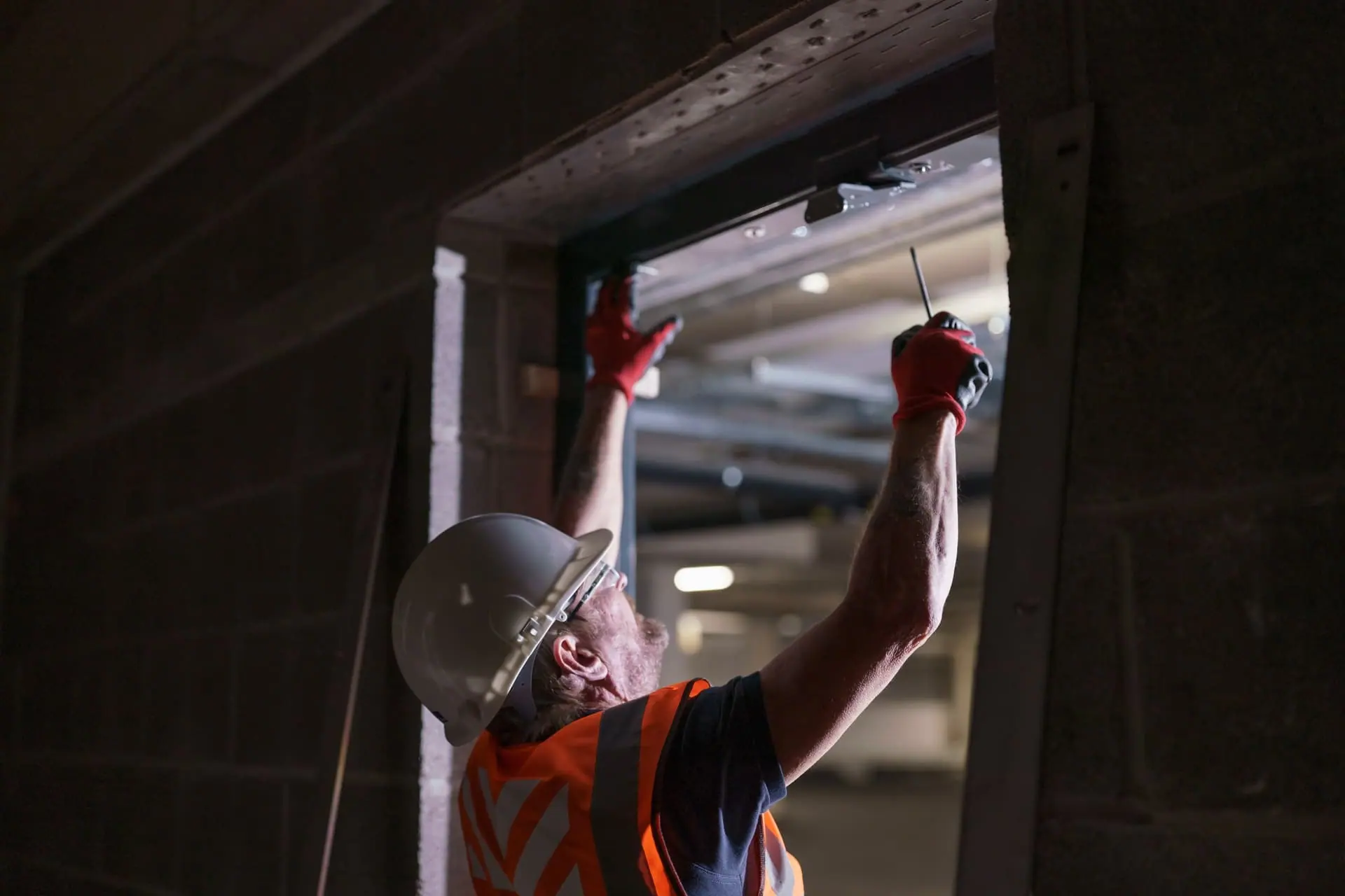 Installer in hard hat and hi-vis fitting hardware to the top of a door frame