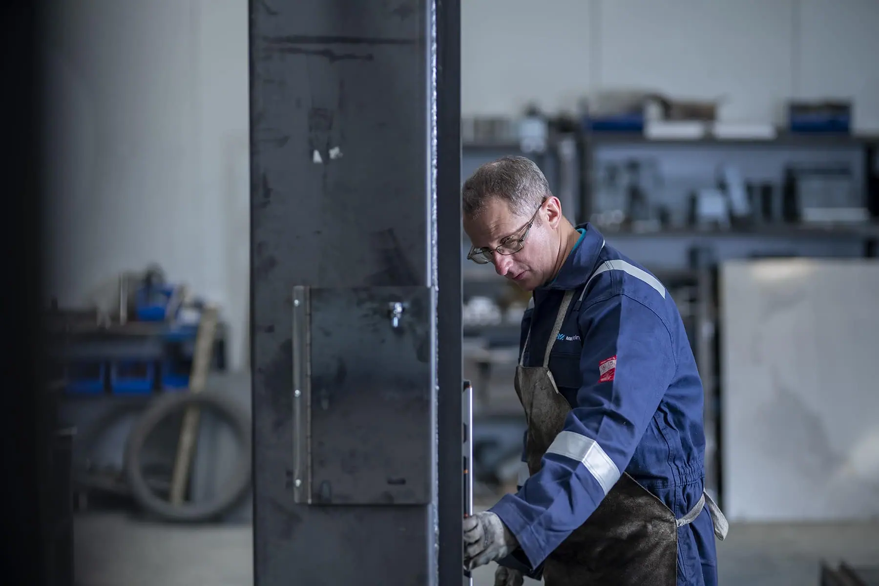 Engineer in overalls and apron checking a steel blast door frame in the workshop