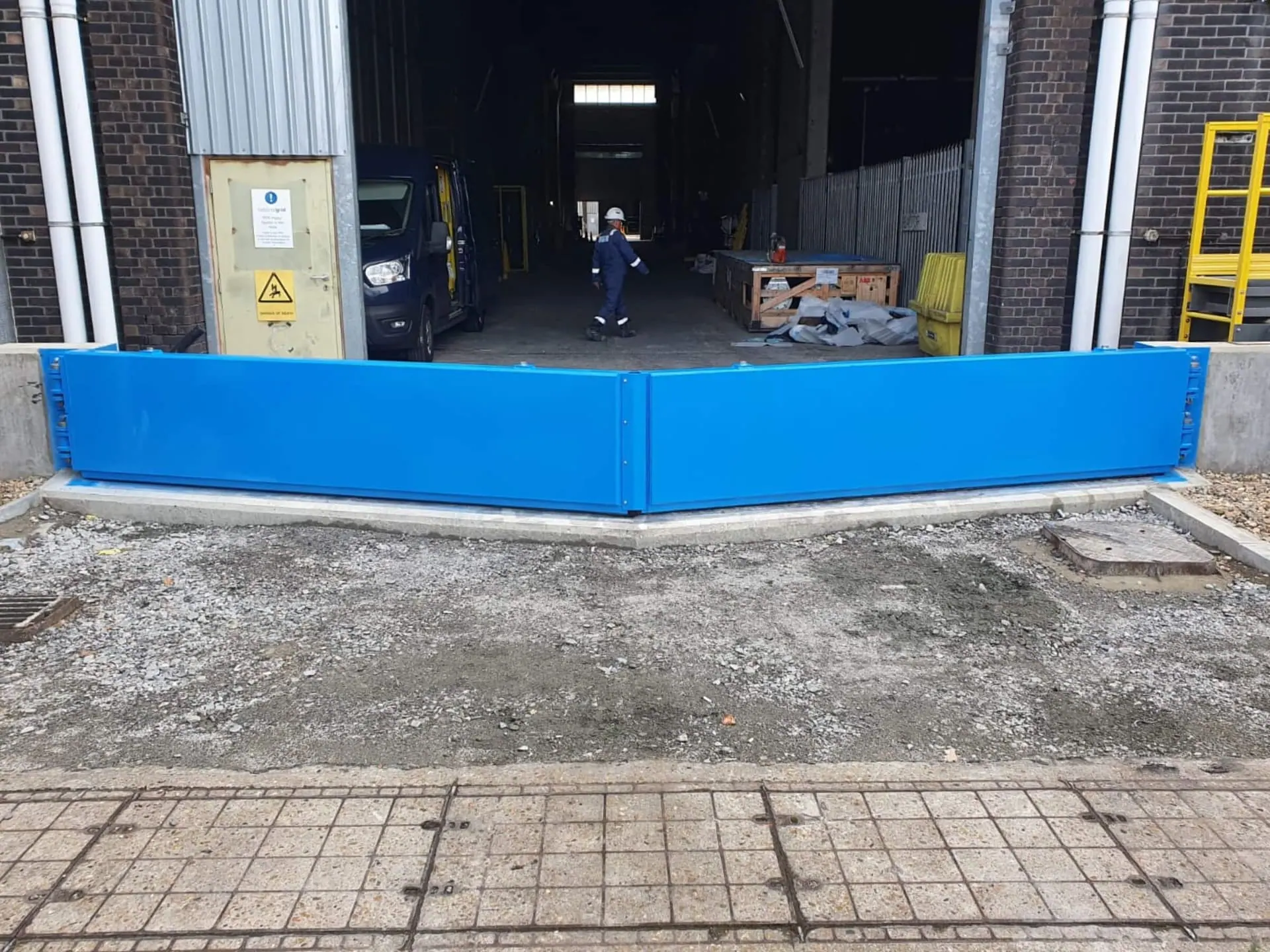 Blue double flood gate closed across a loading bay entrance with a worker walking behind