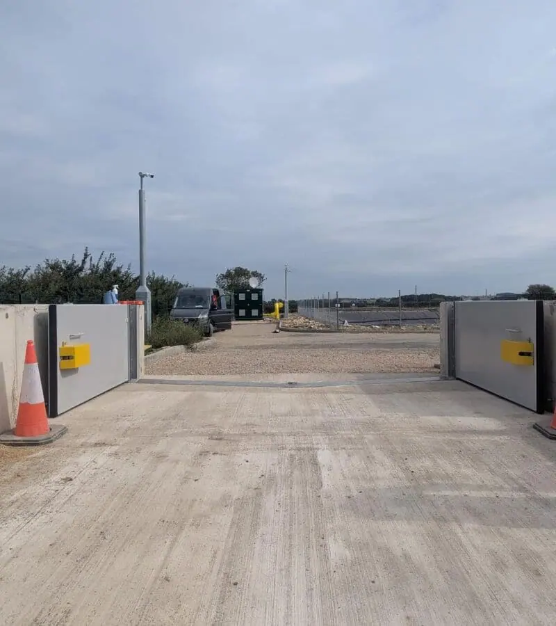 Two grey bund containment gates with yellow lock boxes open either side of a concrete road