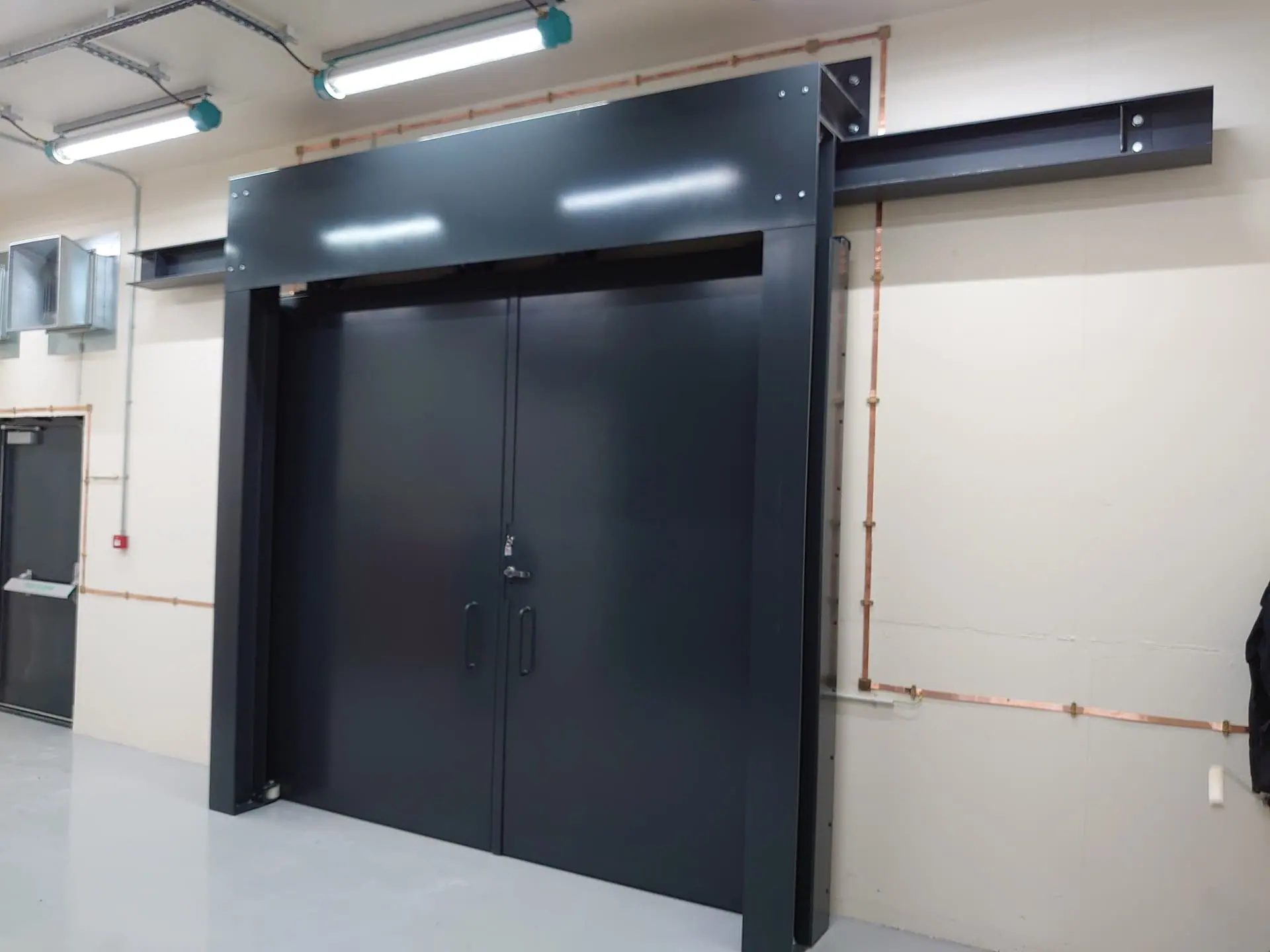 Dark grey double blast doors in a steel frame with overhead sliding beam