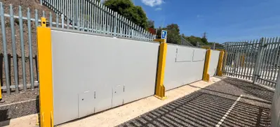 Grey flood gate panels with yellow support posts running beside palisade security fencing